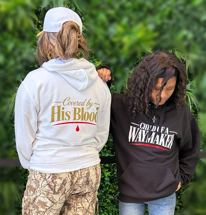 Close-up of two models in white and black WAYMAKER hoodies against a softly blurred green wall