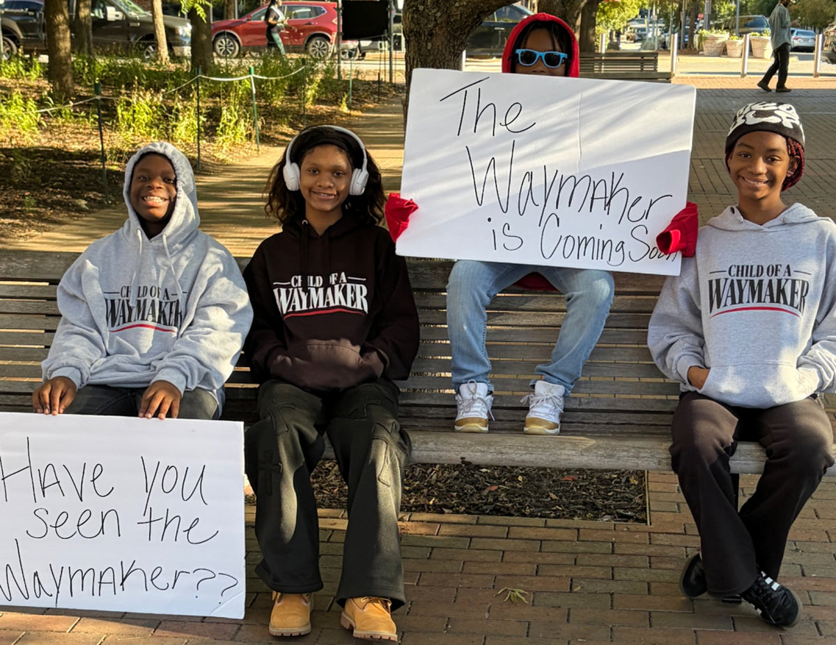 Kids wearing WAYMAKER hoodies on a bench with handwritten Waymaker signs